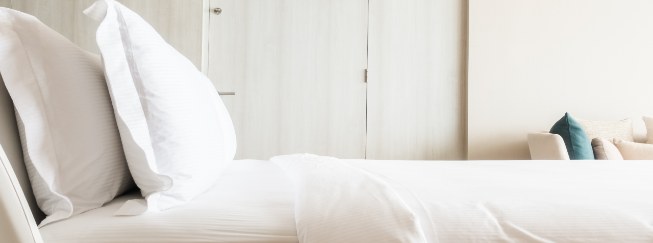 Photo d'un lit vu de côté avec une couette et deux oreillers blancs illustrant le confort dans la prise de contact avec les experts Vitaliterie